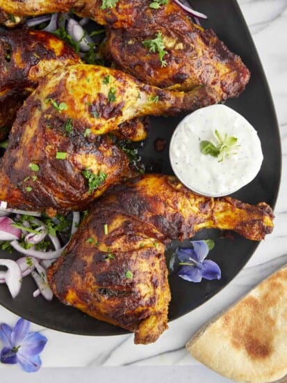 chicken tandoori legs on a plate with tzatziki on the side