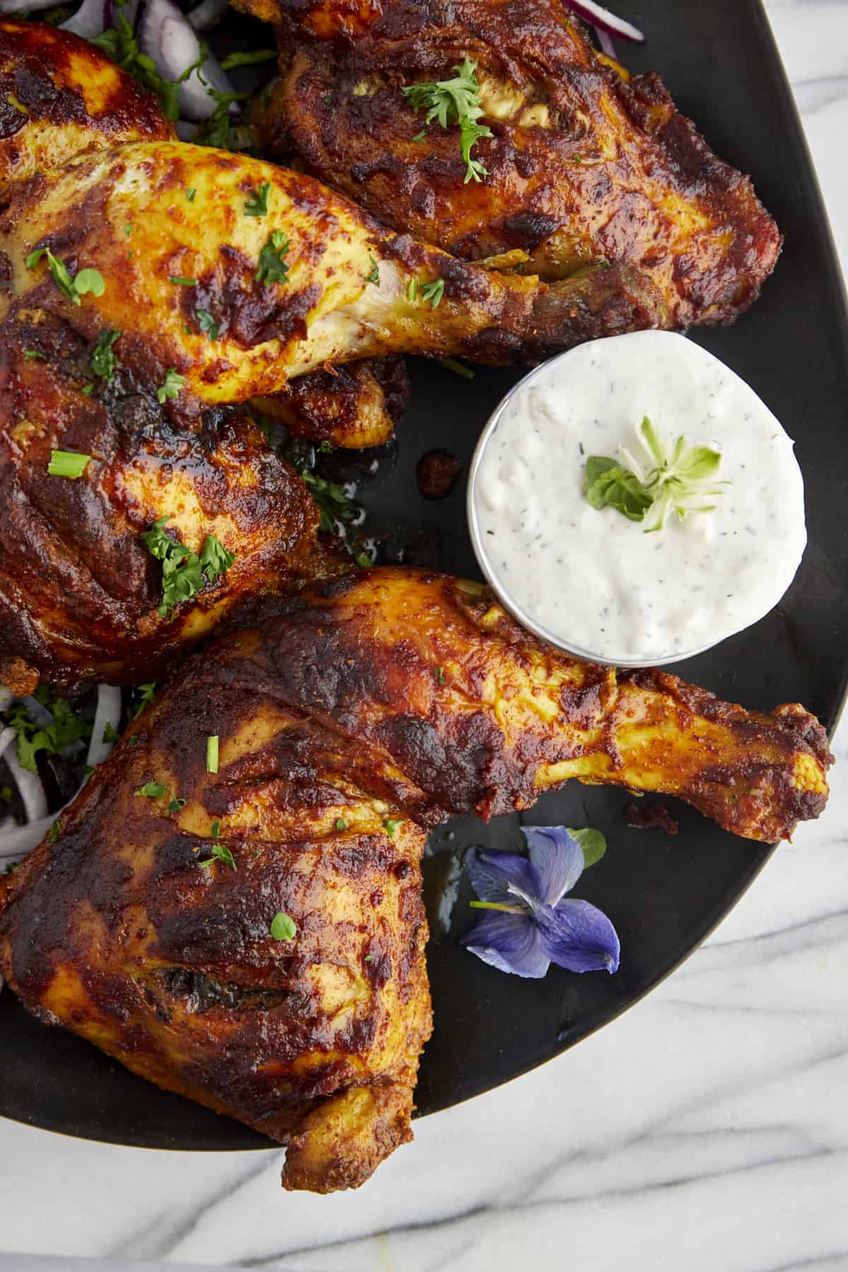 baked chicken tandoori legs on a plate with tzatziki on the side