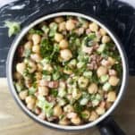 a bowl of chickpea and cucumber tahina salad topped with fresh parsley