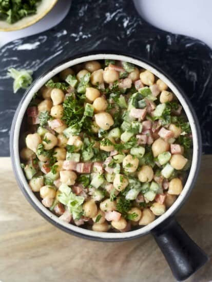 a bowl of chickpea and cucumber tahina salad topped with fresh parsley