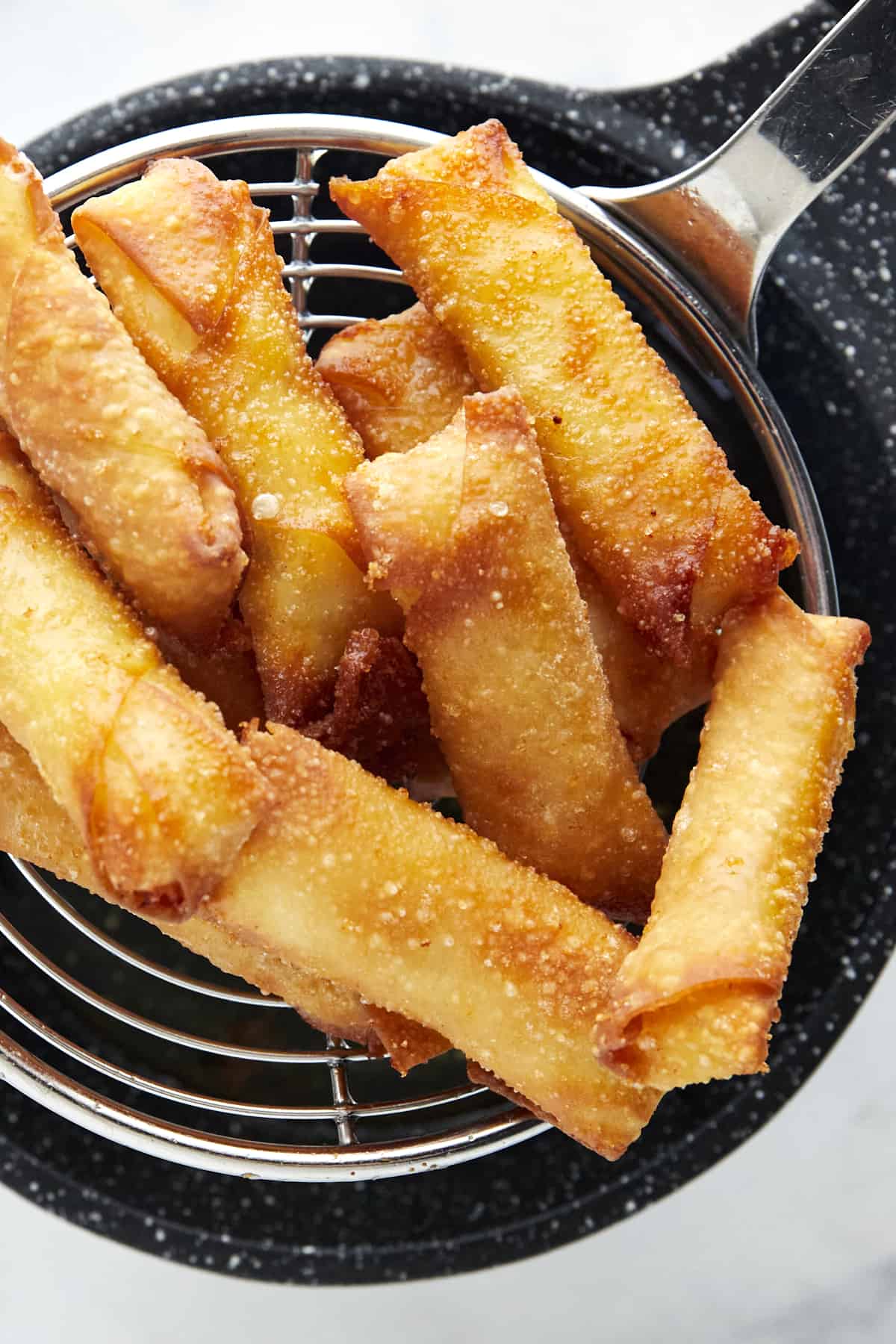 fried feta rolls being lifted from a fryer