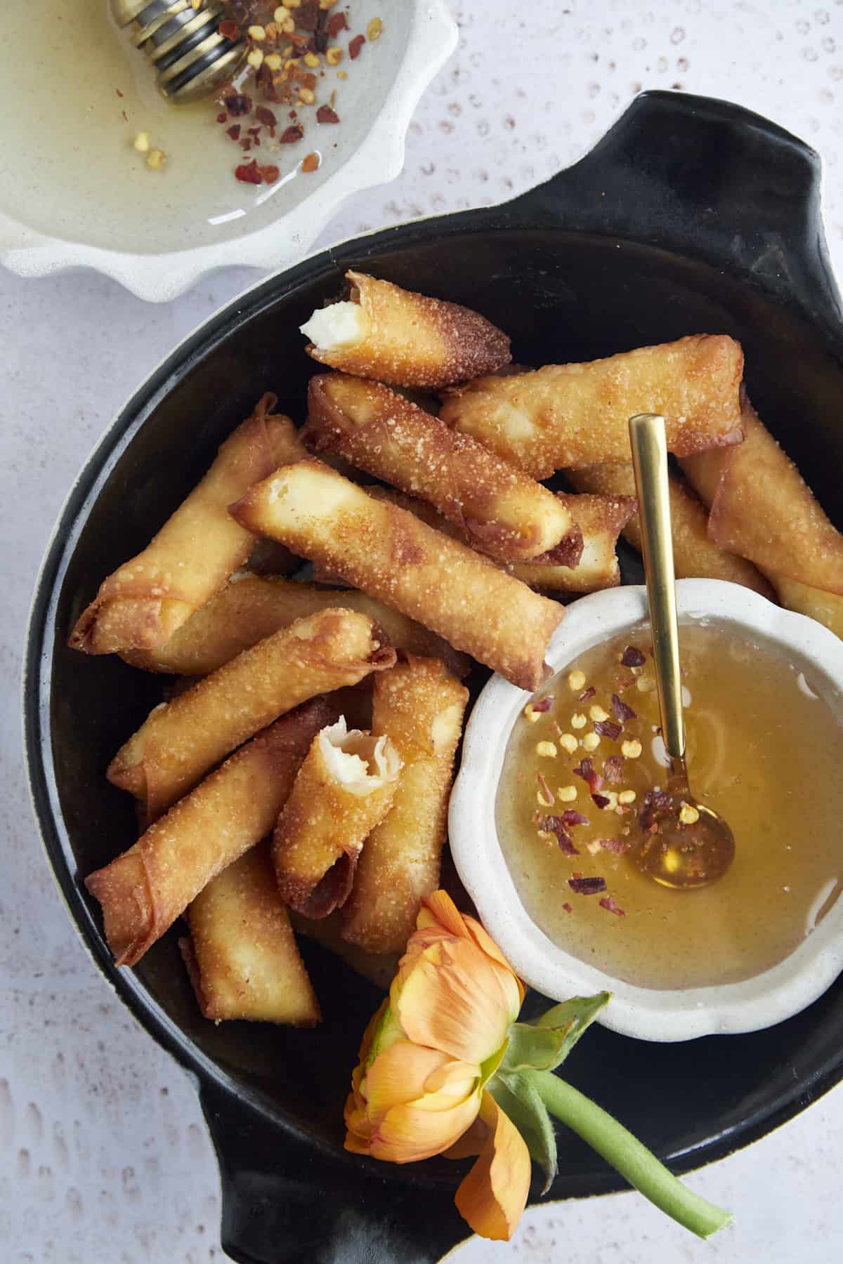 a basket of fried feta rolls with hot honey on the side