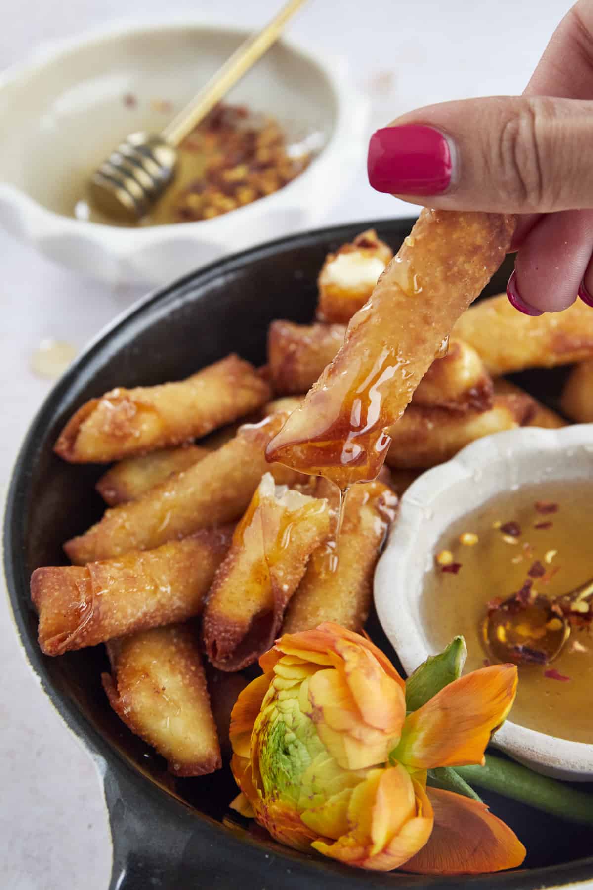 a hand dipping a fried feta egg roll into hot honey