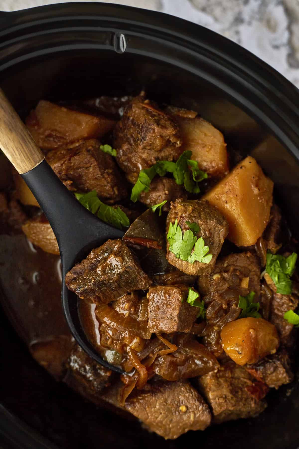 A spoon lifting a scoop of Middle Eastern beef stew from a crockpot. 