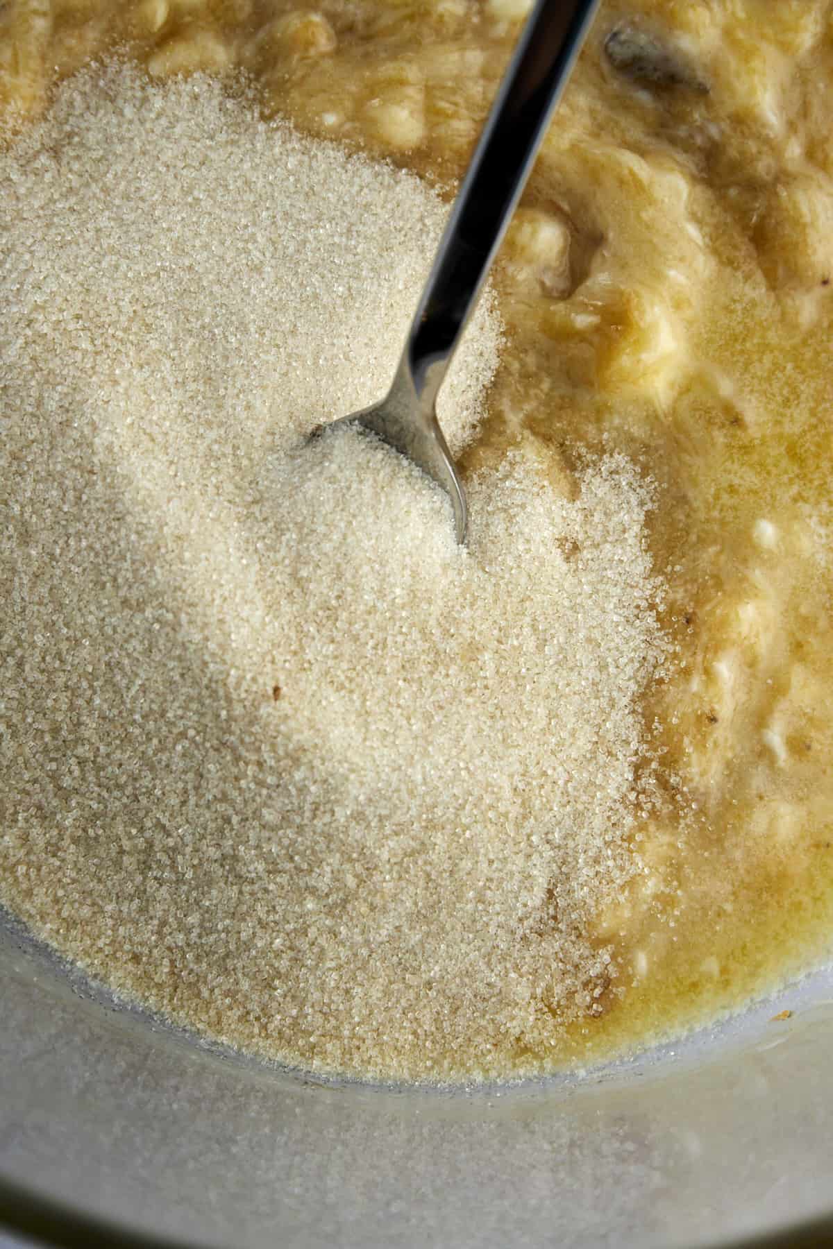 sugar being stirred into mashed bananas for banana bread