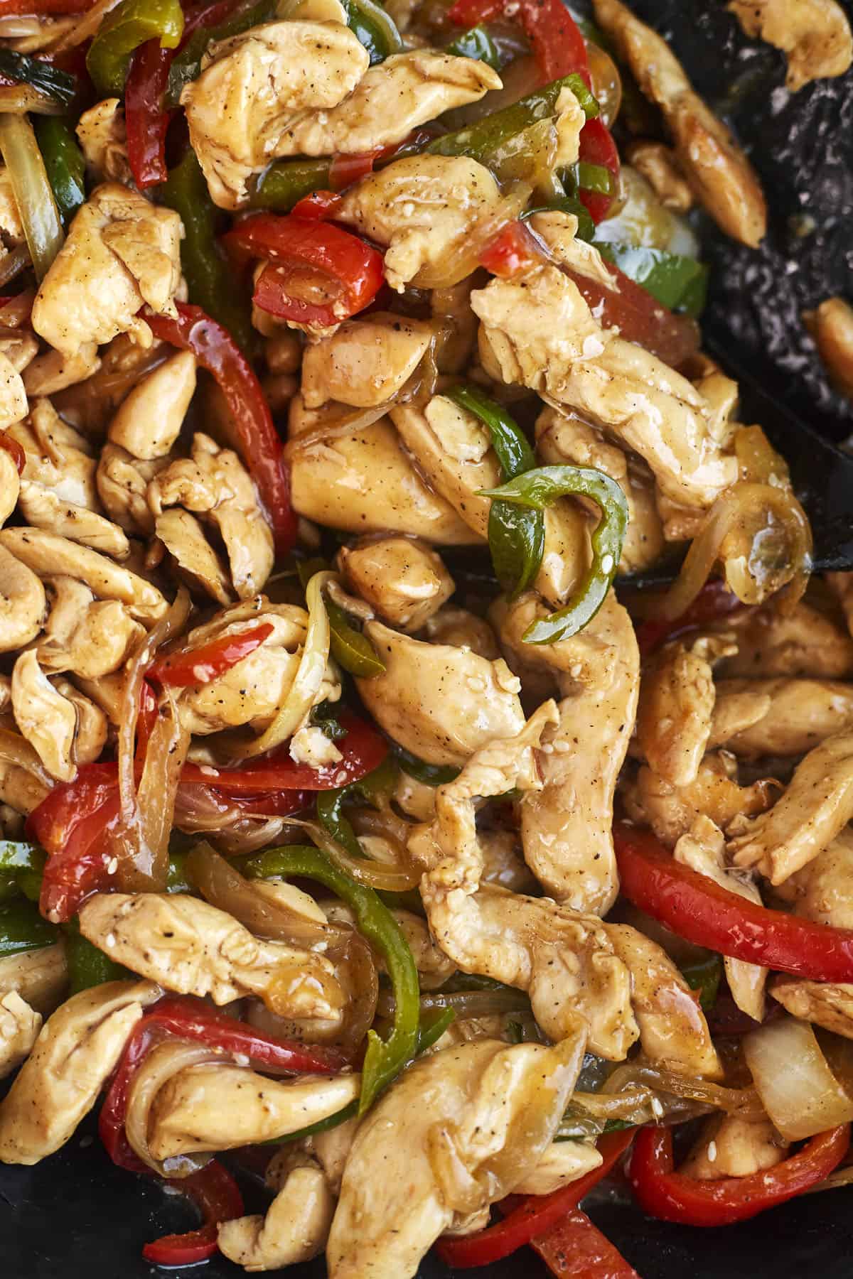 close up image of stir fry chicken, peppers, and onions in a skillet