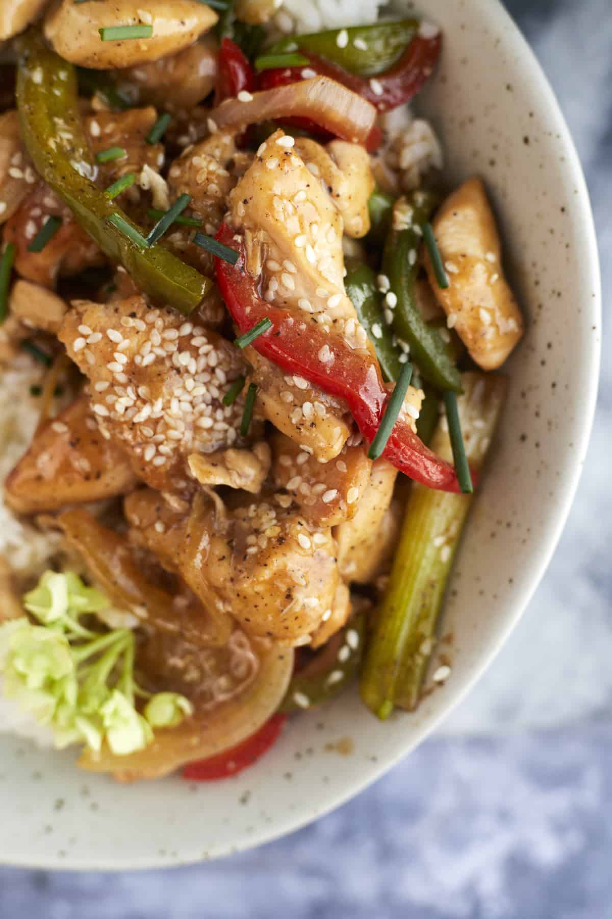 a bowl of black pepper chicken over rice topped with sesame seeds