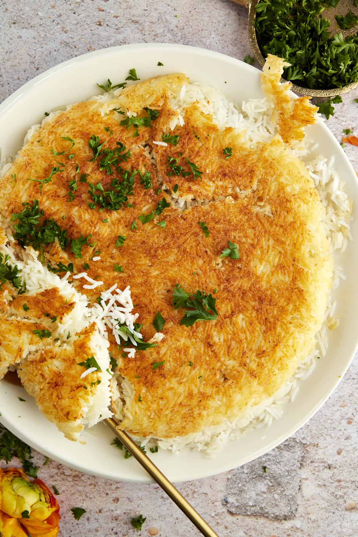 a plate of Persian rice topped with fresh herbs with a portion being scooped up 