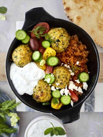 a skillet with rice, Greek meatballs, cucumber, tomatoes, and tzatziki