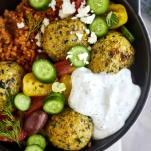 greek meatballs in a skillet with peppers, cucumber, and tzatziki