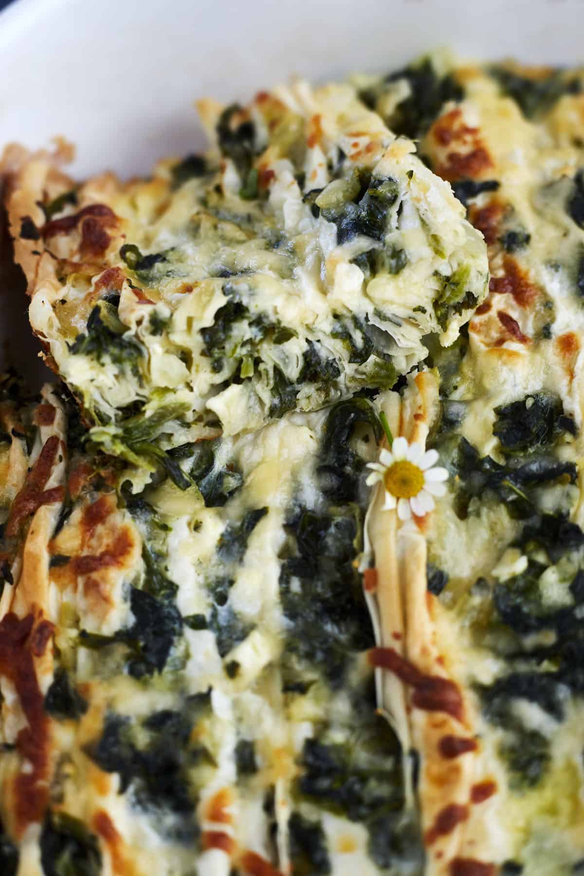 a slice of easy spanakopita recipe being lifted from a casserole dish.