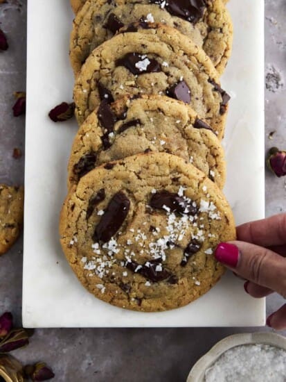 a hand grabbing a cookie from a plate of tahini chocolate chip cookies