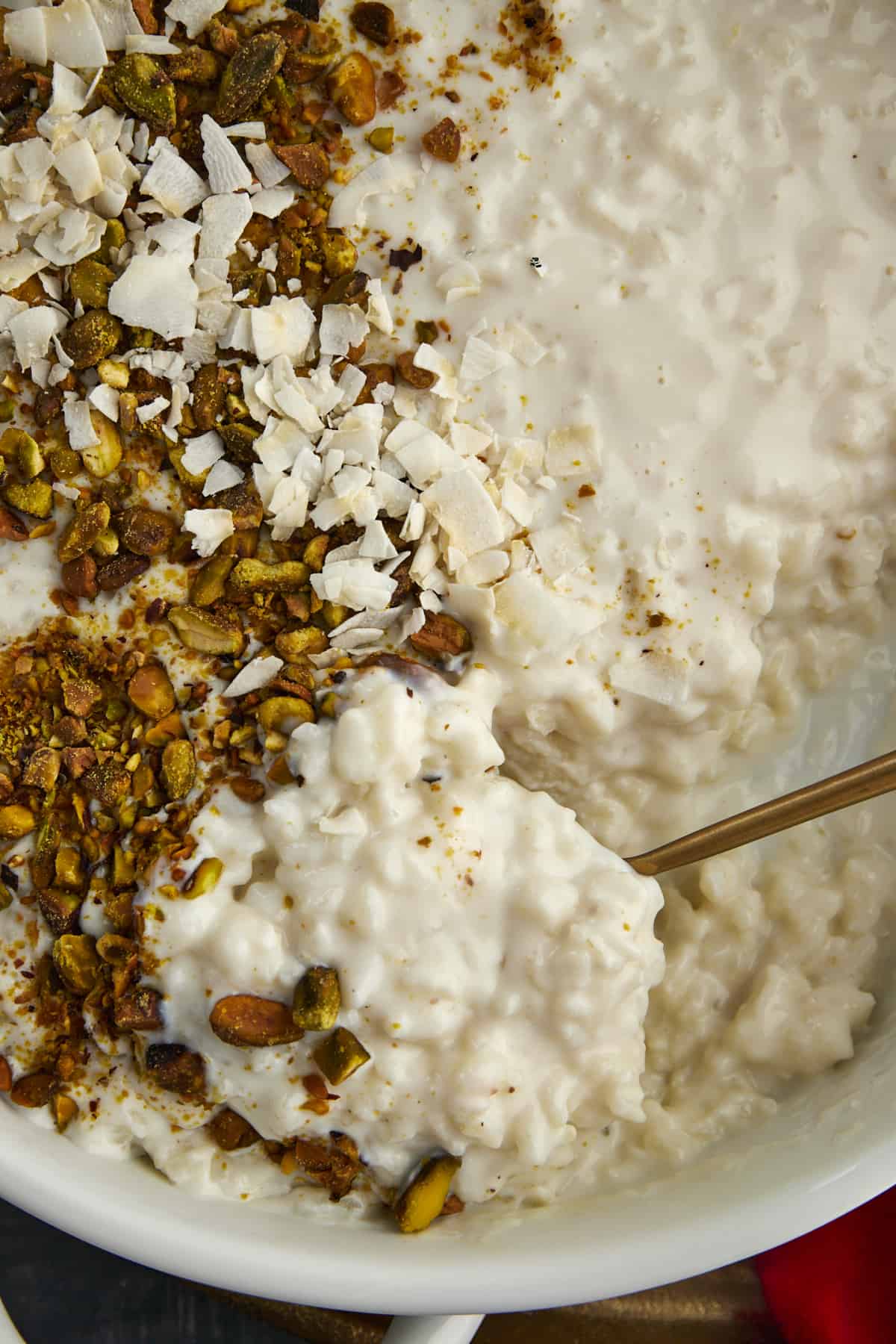close up image of a spoon scooping up coconut rice pudding topped with pistachios and coconut flakes