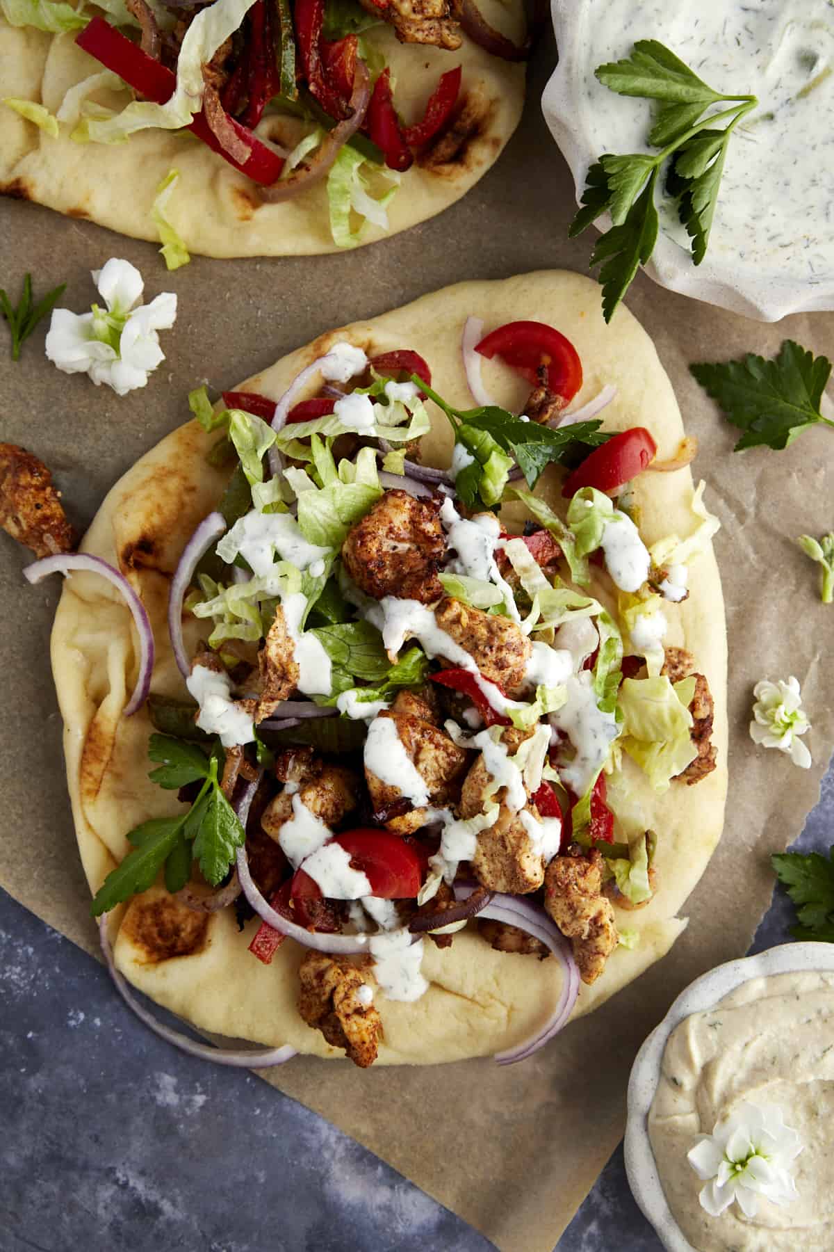 a naan bread chicken shawarma wrap topped with lettuce, red onion, parsley, and tzatziki