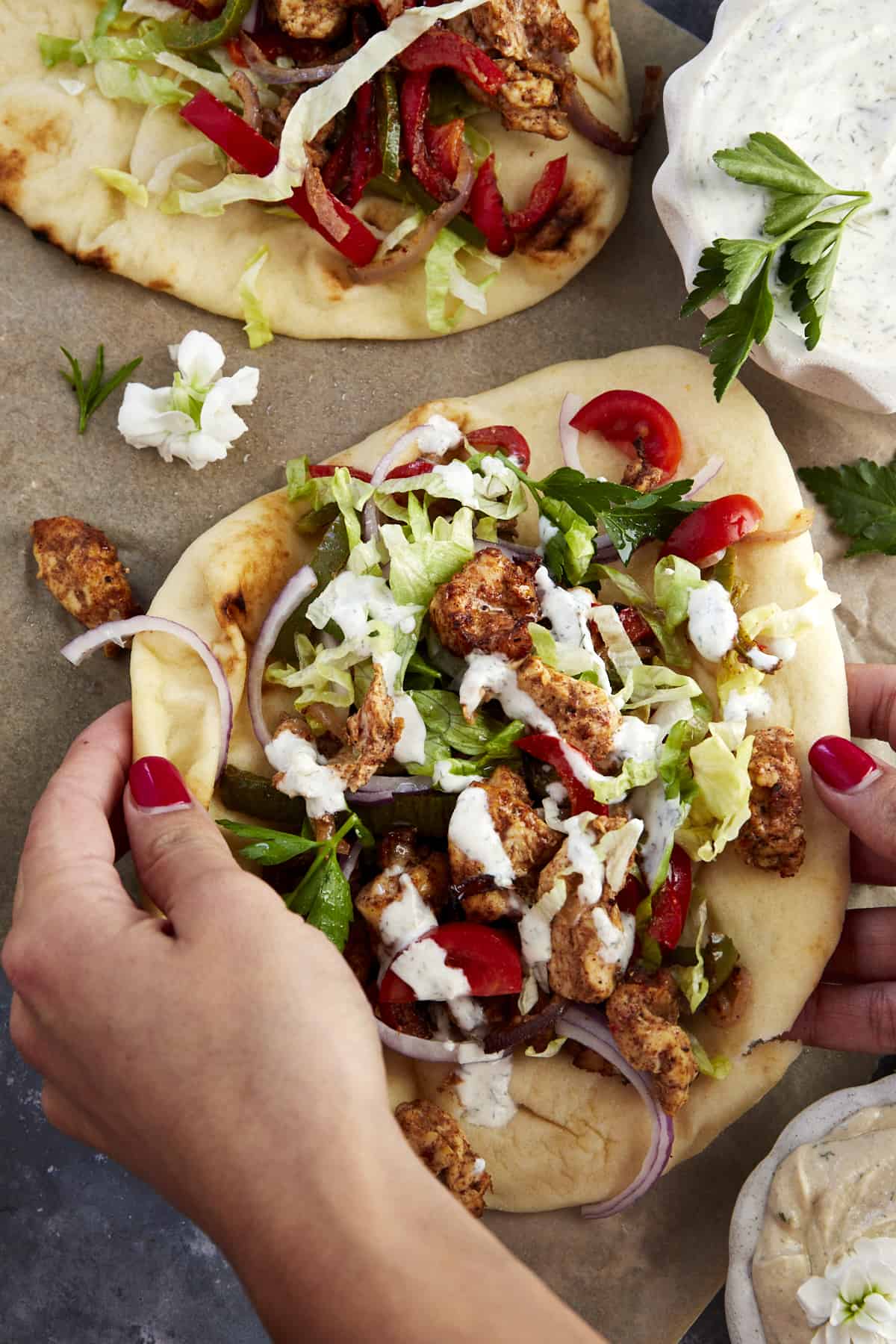 Two hands folding an air fryer chicken shawarma wrap topped with tzatziki. 