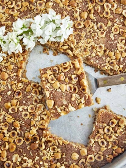 A piece of semolina cake being lifted from a sheet pan.