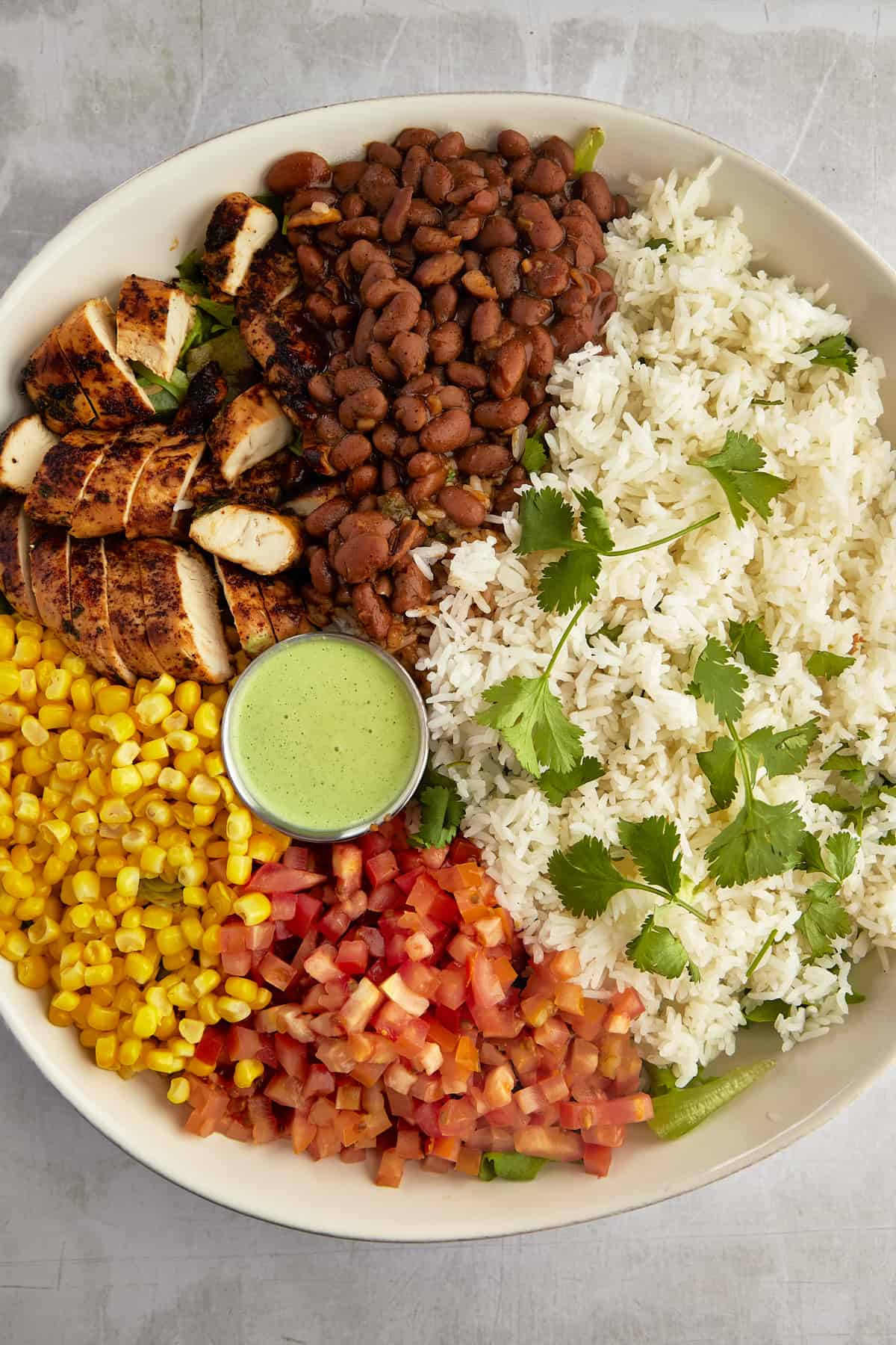 a bowl of southwest chicken salad with rice, beans, chicken, corn, tomatoes, and cilantro dressing in the center