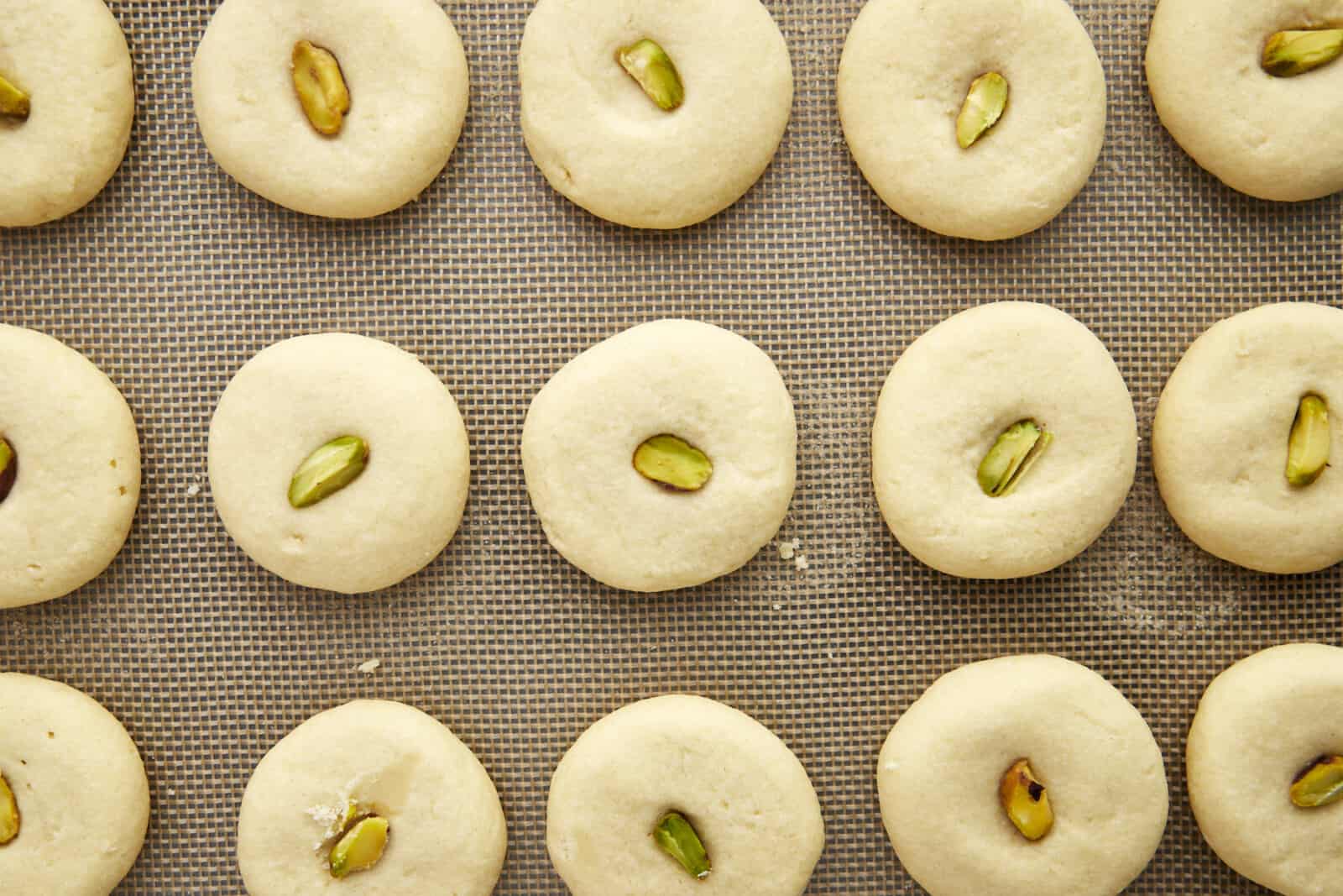 Baked graybeh cookies topped with pistachio halves on a baking sheet. 