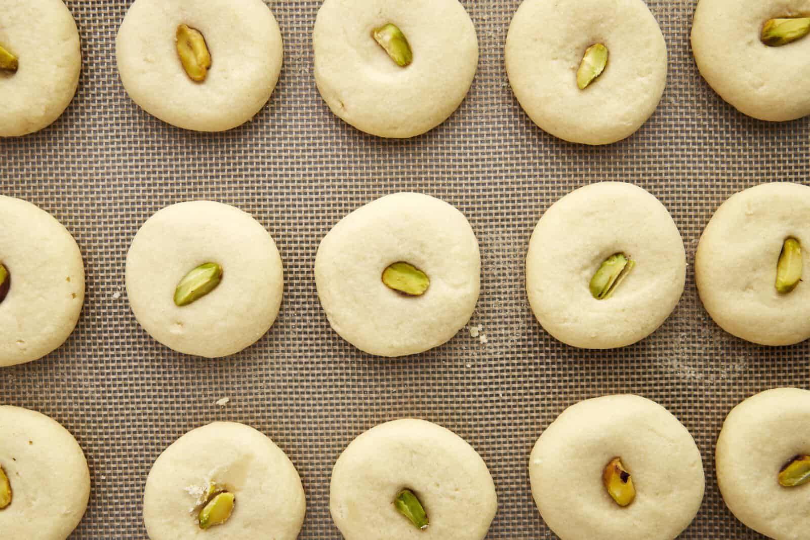 Baked graybeh cookies topped with pistachio halves on a baking sheet.