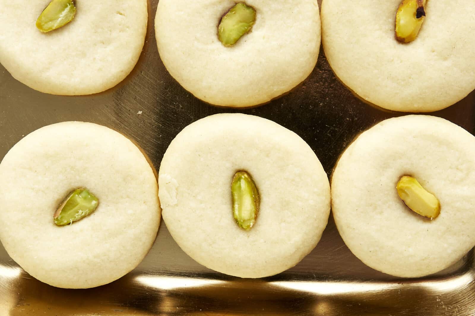 Close up image of ghraybeh cookies topped with pistachio halves. 