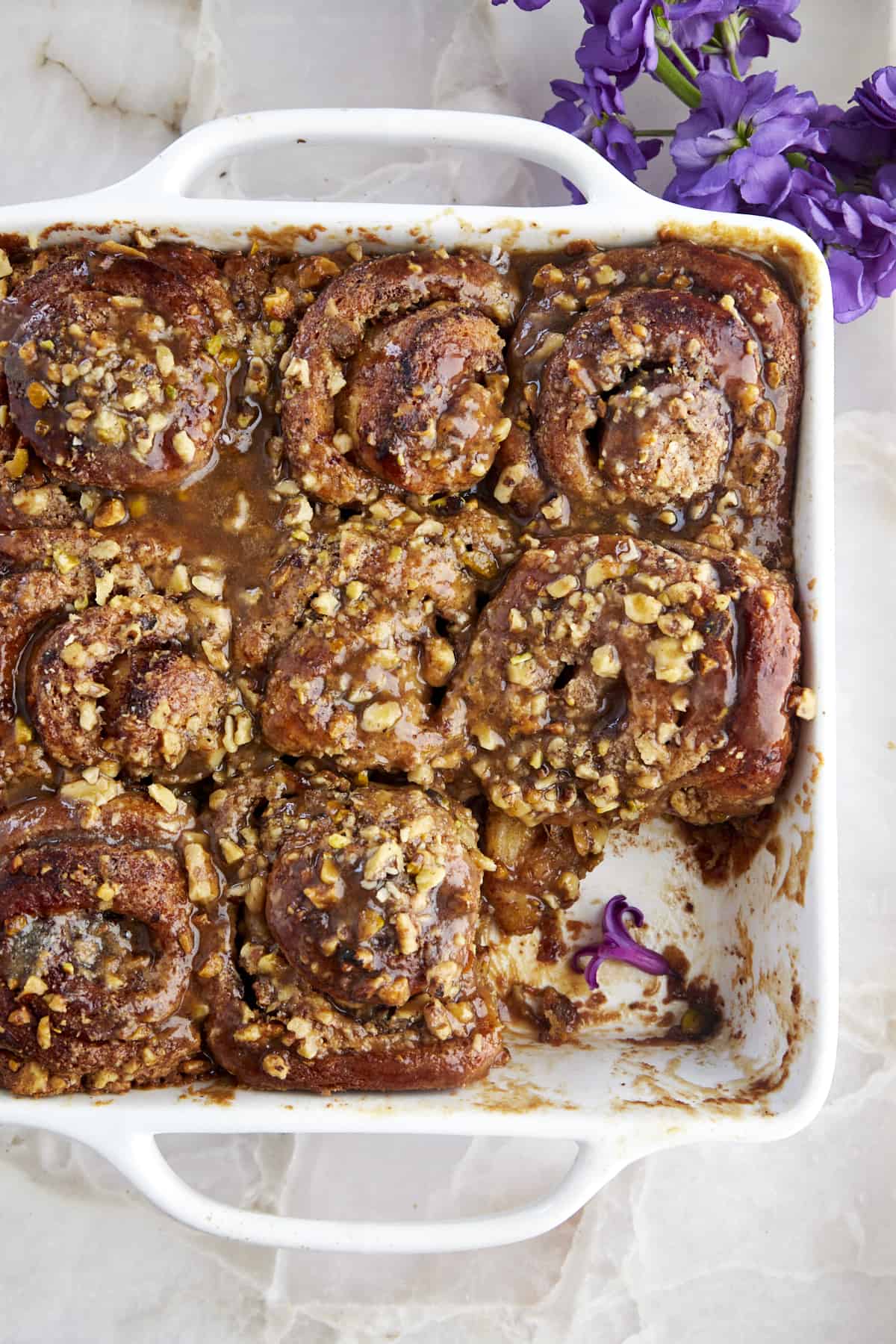 a baking dish of cinnamon rolls with nuts with a cinnamon roll missing