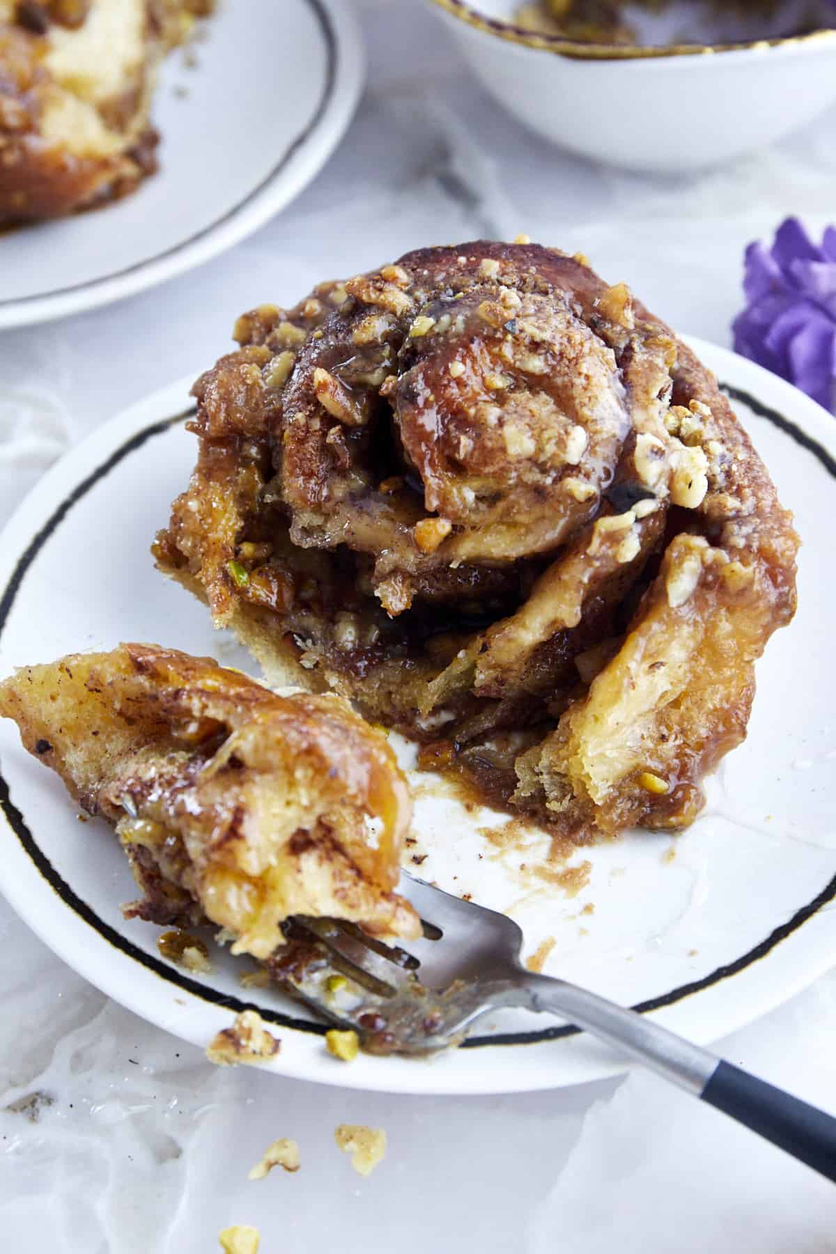 a fork taking a bite from a pistachio walnut cinnamon roll on a plate