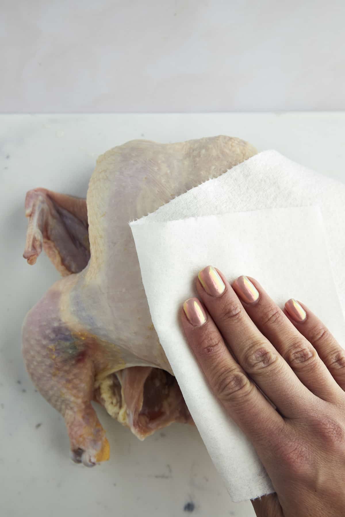 A hand using paper towels to pat the chicken dry. 