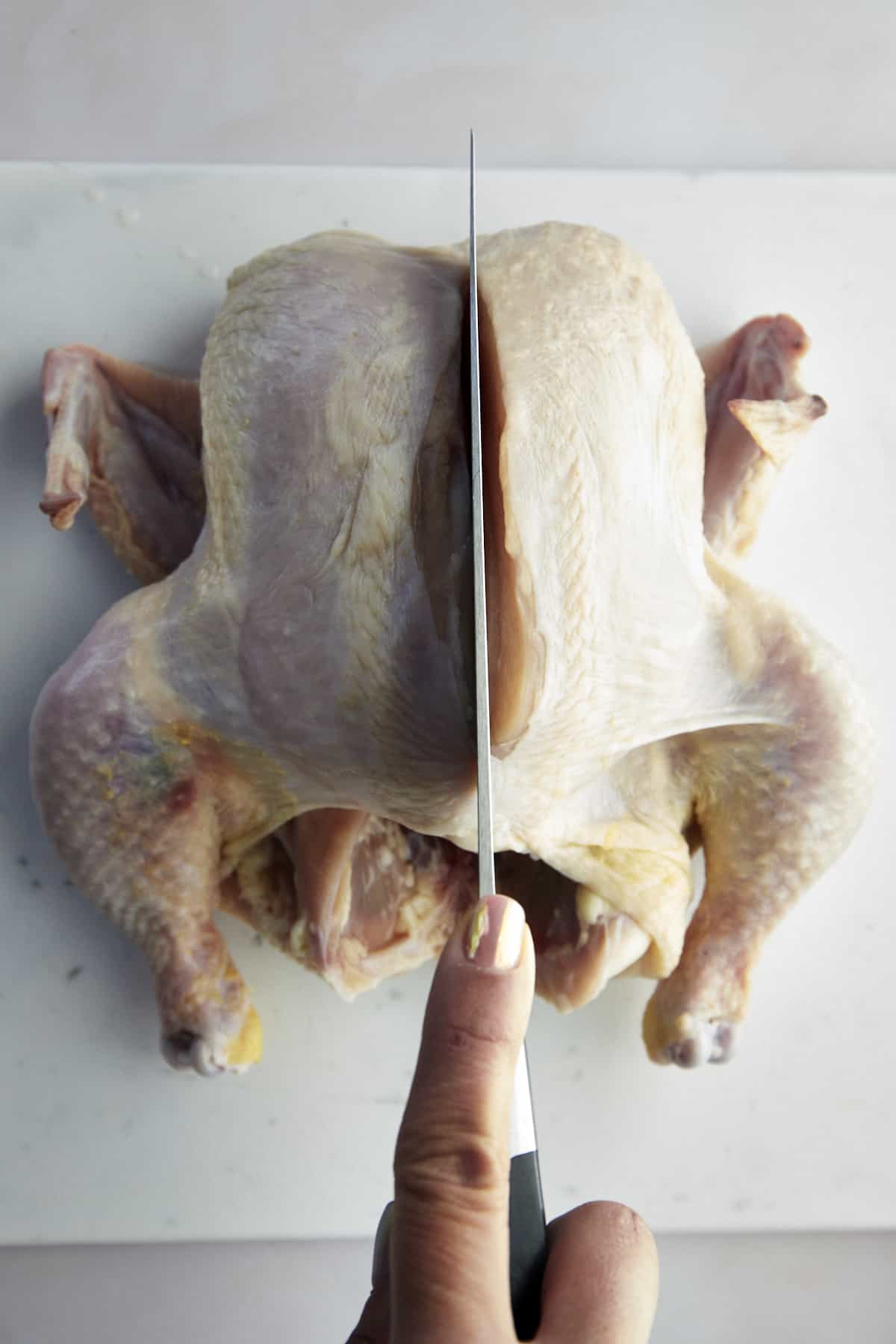 A knife slicing down the backbone of the chicken. 