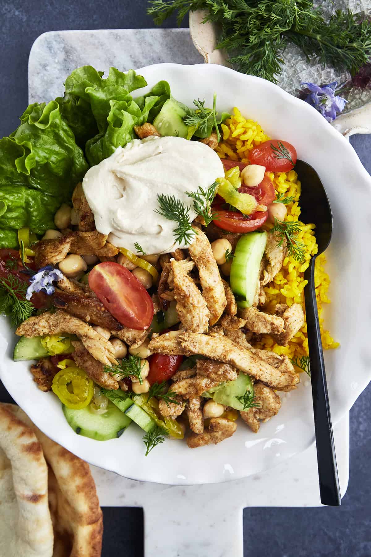 A bowl of chicken shawarma with rice, veggies, and hummus. 