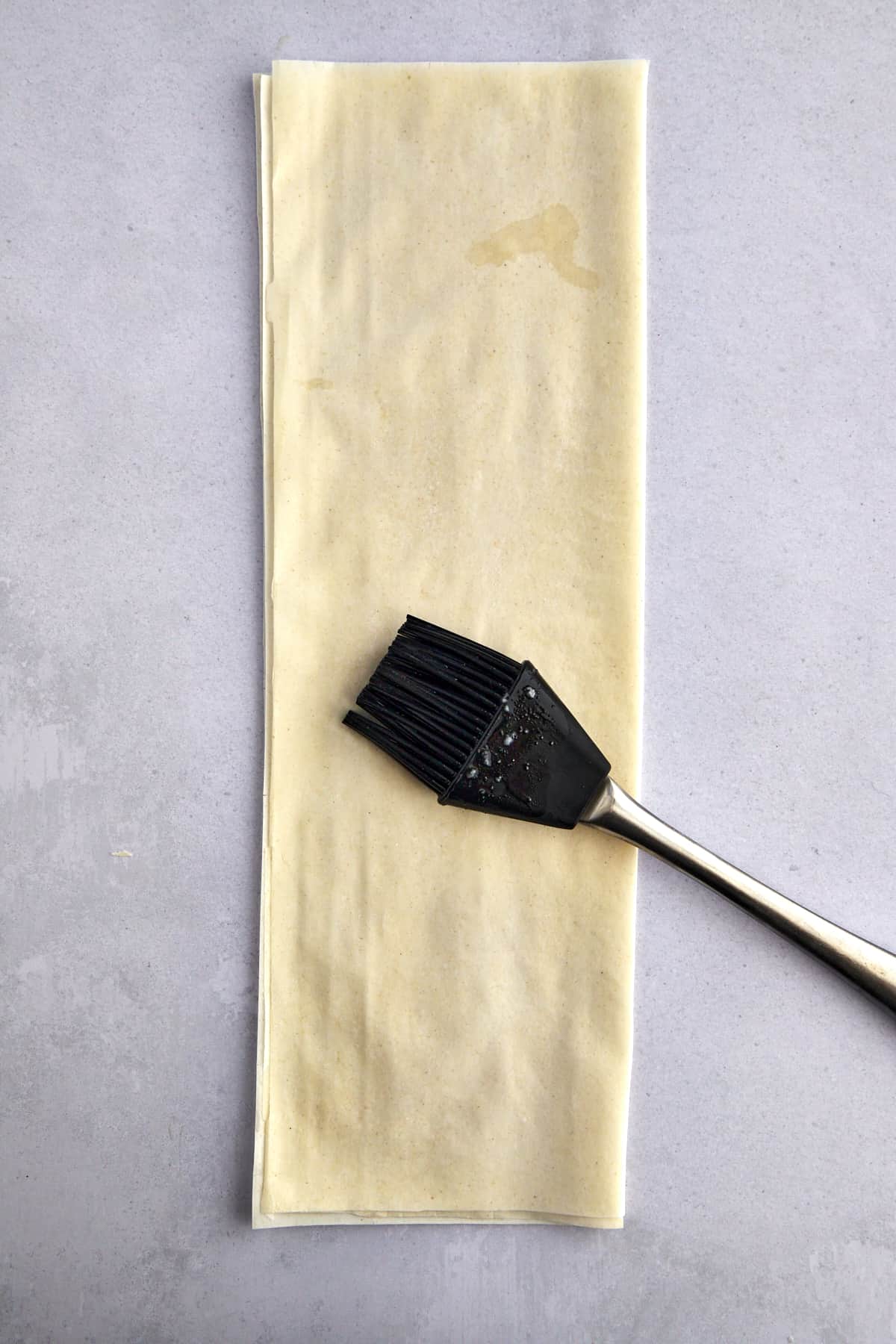 A pastry brush spreading dough over layered phyllo sheets. 