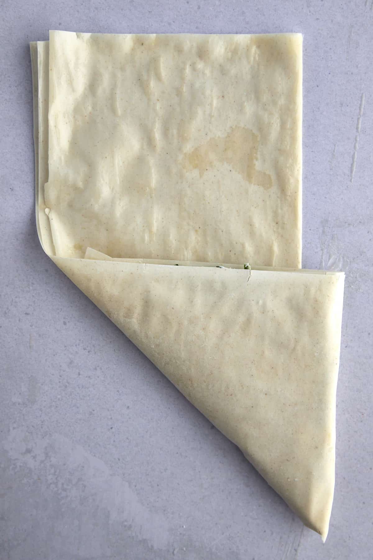 Raw phyllo dough being folded into a triangle. 