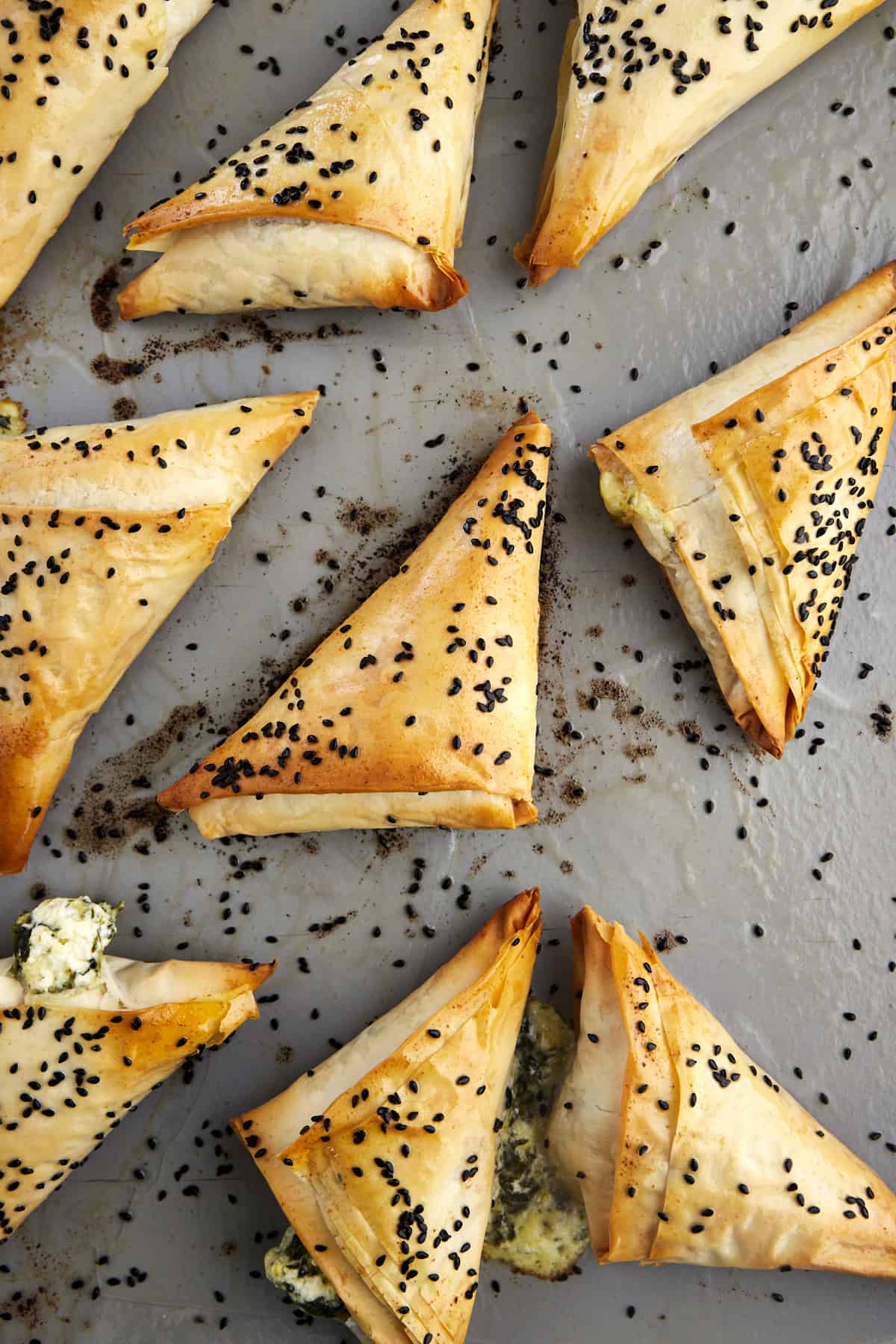 Spanakopita triangles topped with black sesame seeds on a baking sheet. 