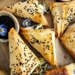Baked spanakopita triangles topped with black sesame seeds.