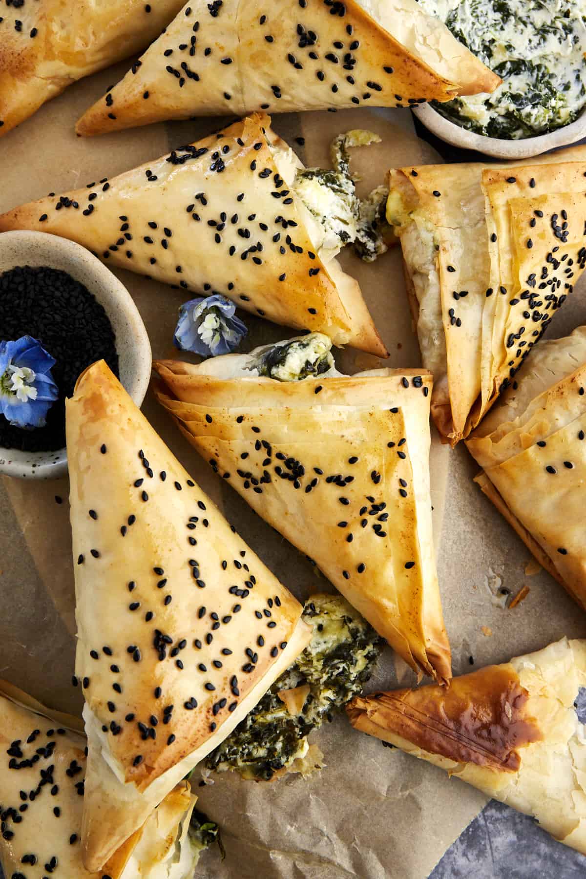 Baked spanakopita triangles topped with black sesame seeds on parchment paper.