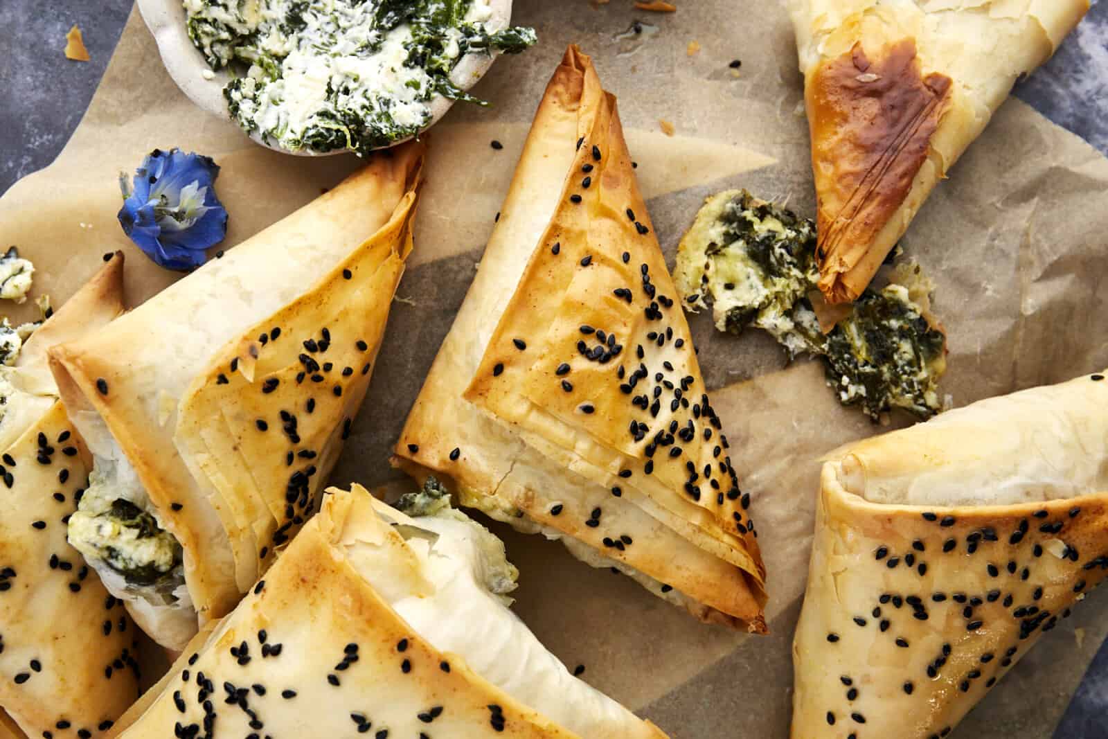 6 spanakopita triangles on parchment paper. 