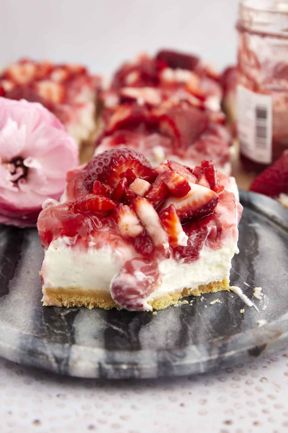 A strawberry cheesecake bar on a plate with a bite taken out. 