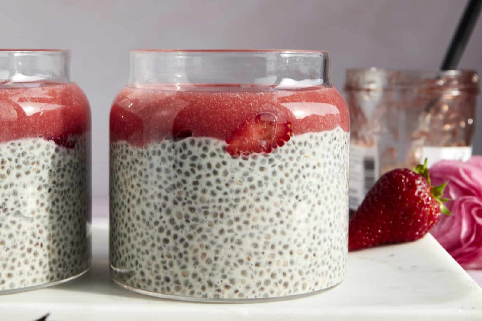 Side view of a jar of strawberry chia pudding topped with strawberry puree and sliced strawberries. 