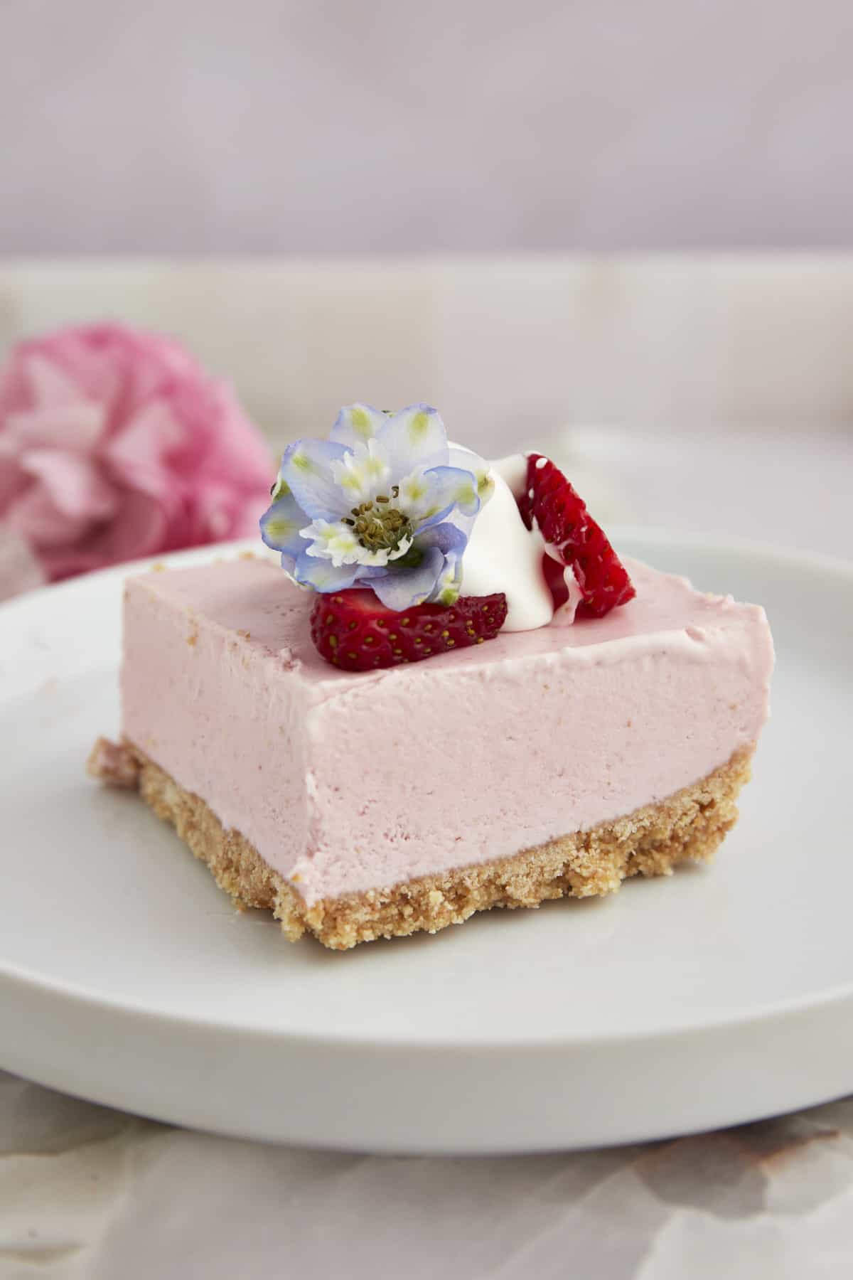 A no-bake strawberry cheesecake square on a plate topped with strawberries and whipped cream. 