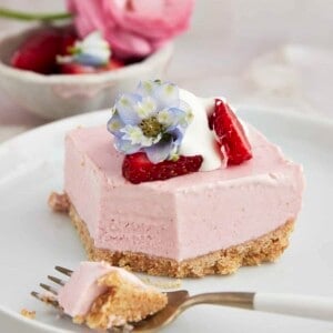 A strawberry cheesecake square on a plate with a fork holding a bite.