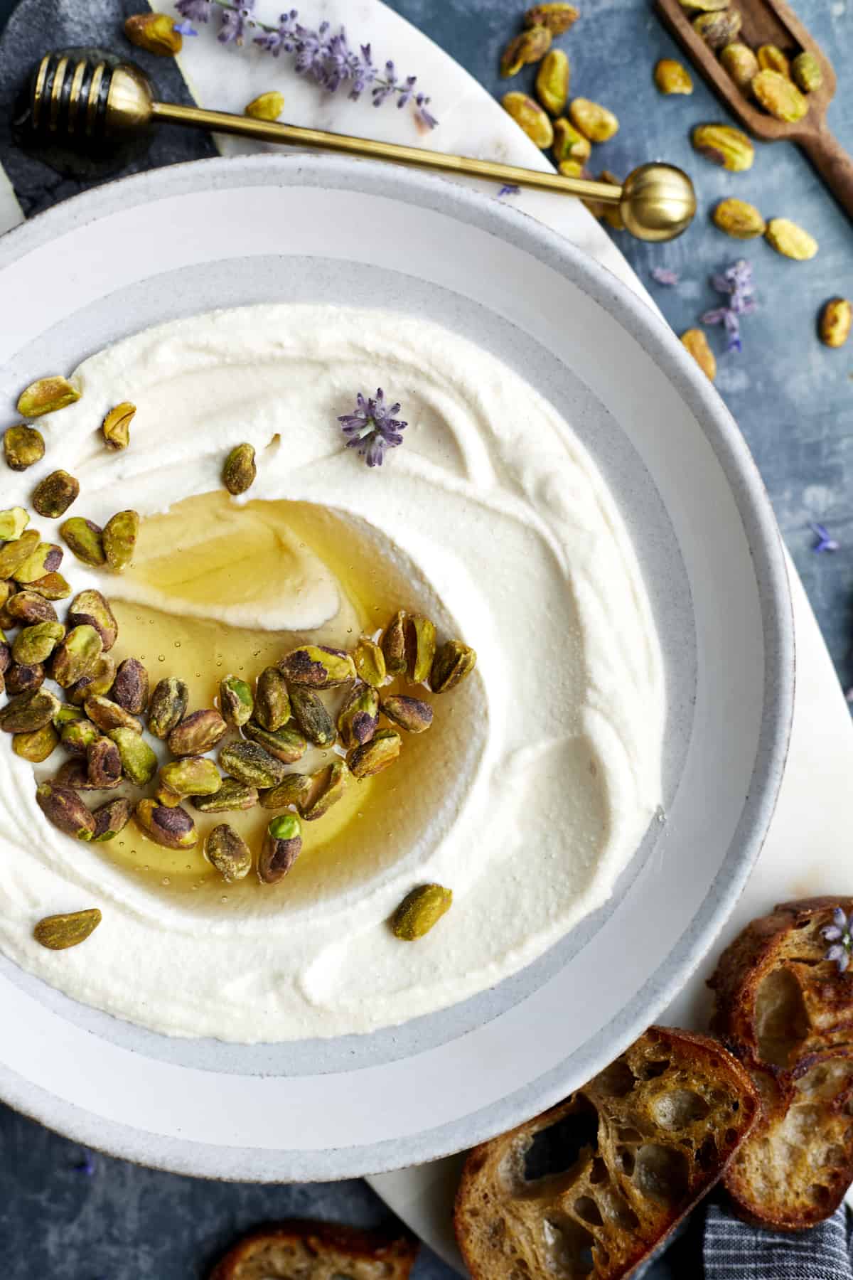 A bowl of whipped ricotta dip topped with roasted pistachios and honey. 