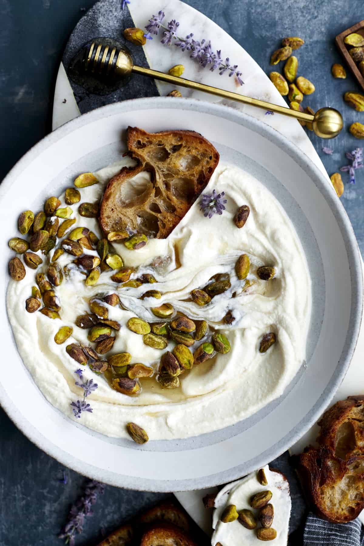 A bowl of whipped ricotta topped with pistachios and honey with a piece of crostini. 