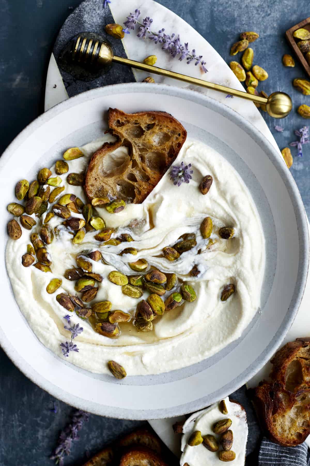A bowl of whipped ricotta topped with pistachios and honey with a piece of crostini.