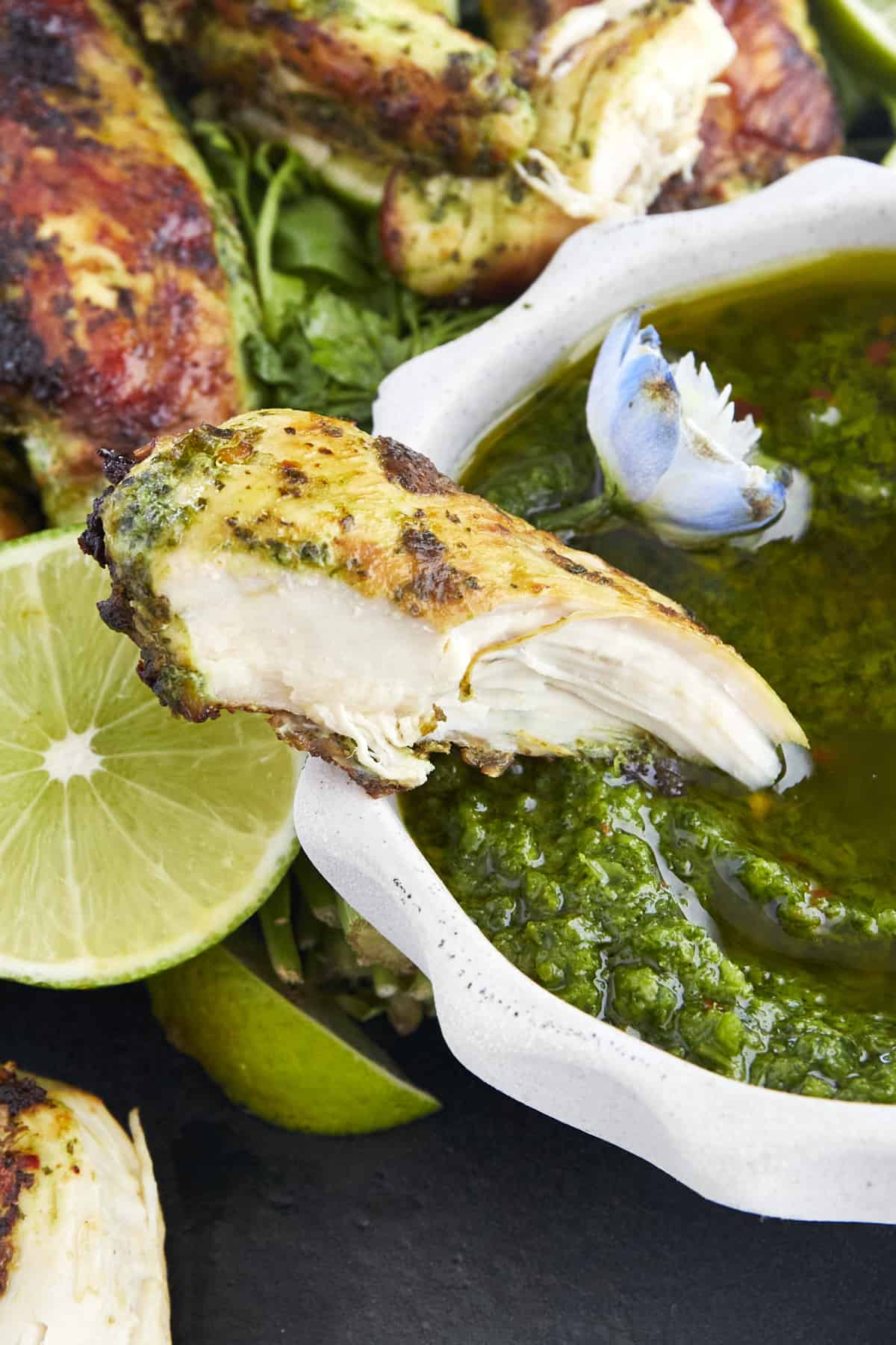 A piece of cilantro lime chicken being dipped in zhoug sauce. 