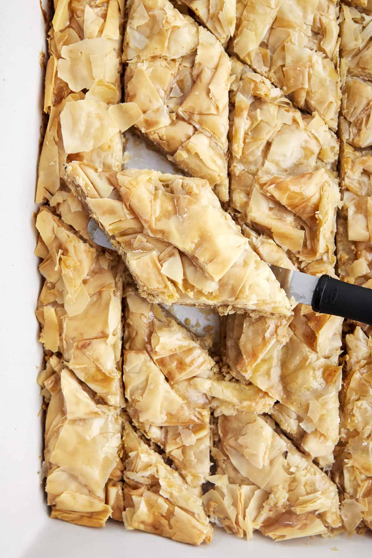 A baking dish full of easy baklava with a piece being lifted with a spatula.