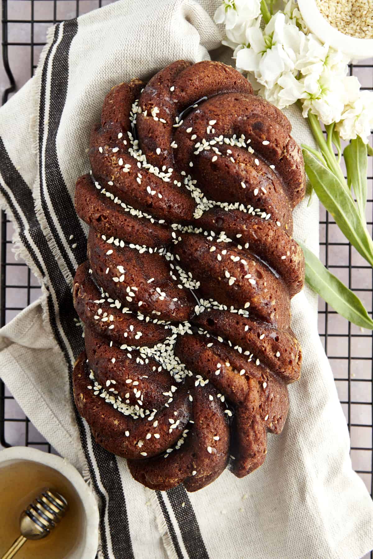 A loaf of tahini banana bread topped with honey and white sesame seeds on a wire rack. 