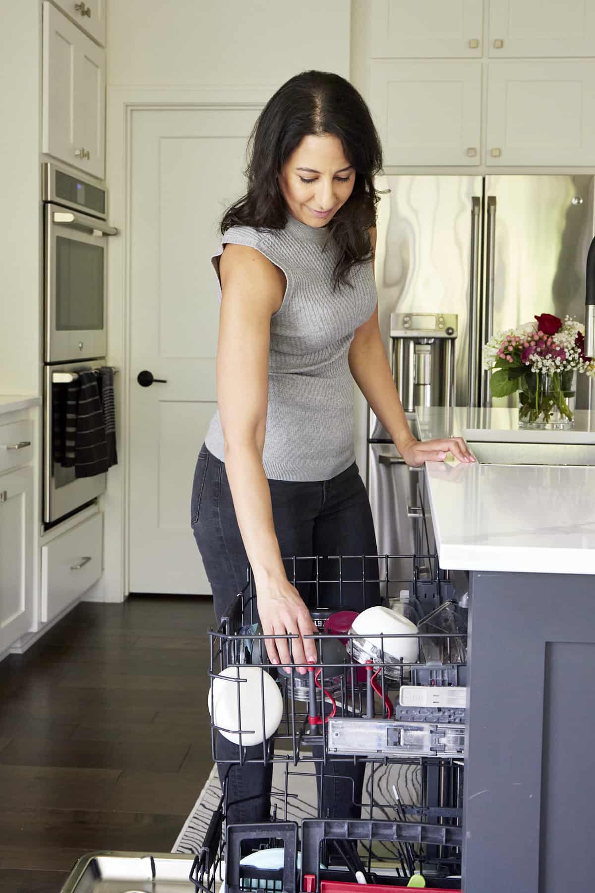 A woman loading various items into the top rack of a dishwasher. 