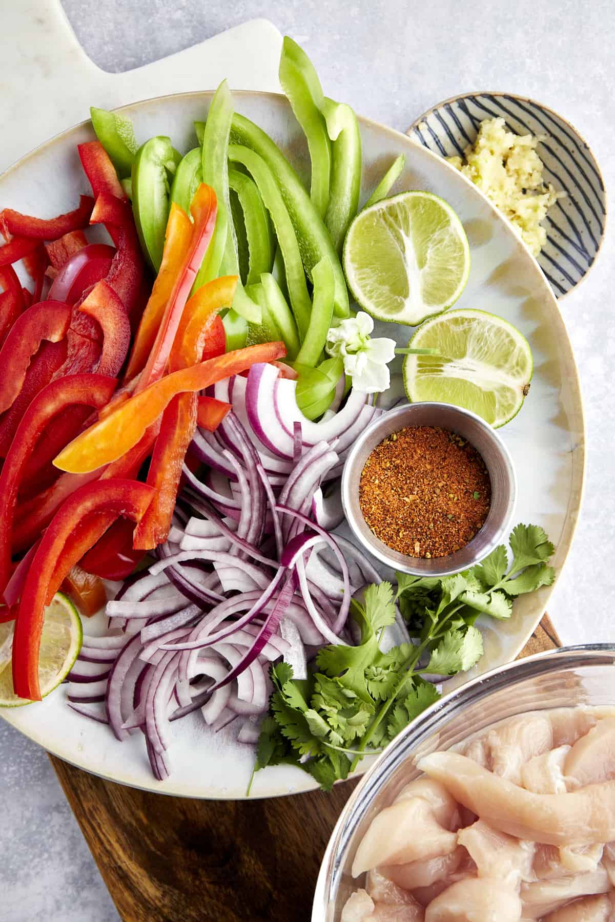 Air fryer chicken fajita ingredients including sliced red and green peppers, red onion, lime halves, taco seasoning, cilantro, and chicken. 