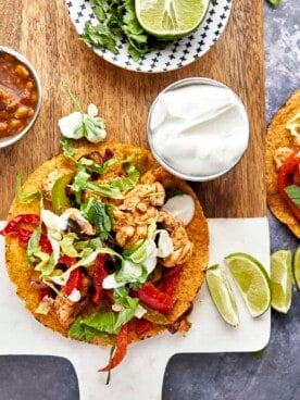 An air fryer chicken fajita taco with sour cream and lime wedges on the side.