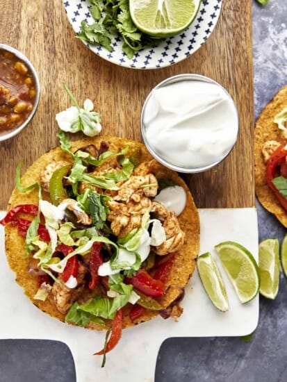 An air fryer chicken fajita taco with sour cream and lime wedges on the side.