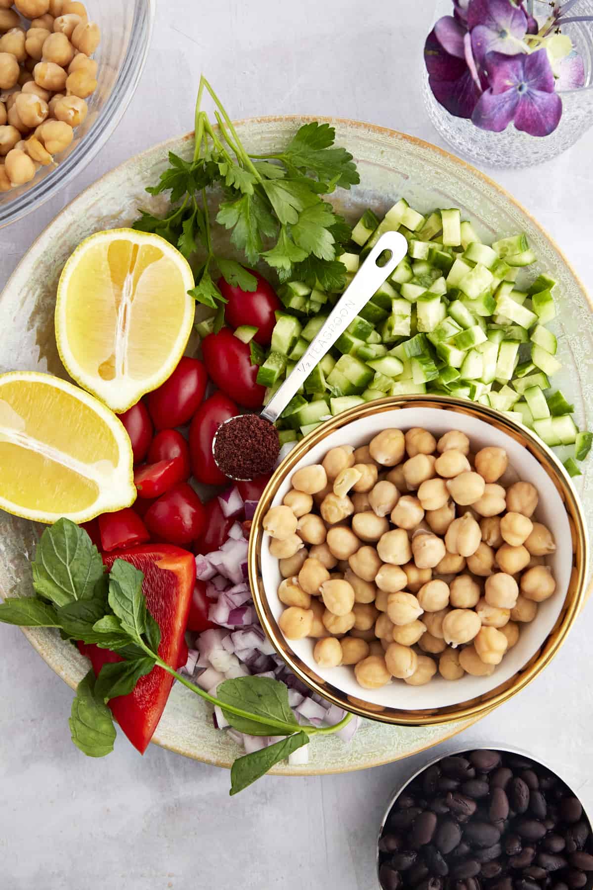 Ingredients for a Balela Salad including chickpeas, black beans, cucumbers, red onion, sumac, lemon, and fresh herbs. 